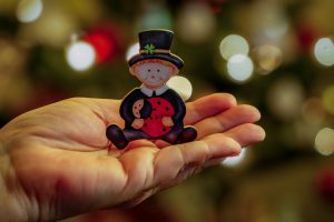 A playful figurine with a ladybug is gently held in hand, surrounded by a festive bokeh background.