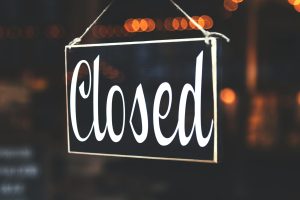 A close-up of a 'Closed' sign hanging against a blurred, bokeh background, creating a warm, inviting atmosphere.