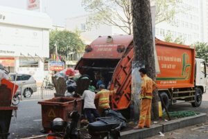 Garbage truck and workers collecting trash in a busy urban street setting.